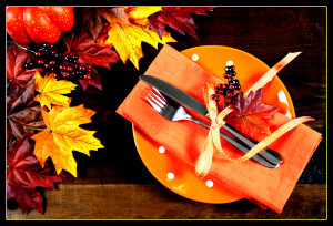 Autumn Fall background with red, brown and yellow leaves, orange pumpkin and monarch butterfly on dark recycled rustic wood table with orange table place setting.