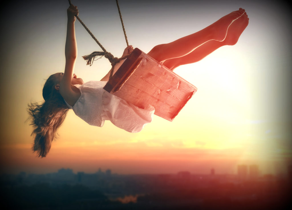 Happy laughing child girl on swing in sunset summer